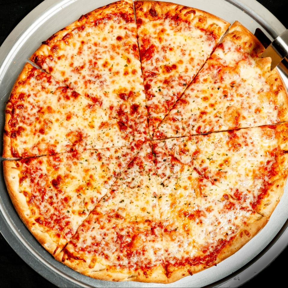 A freshly baked, sliced cheese pizza with herbs on a metal pan, ready to be served.