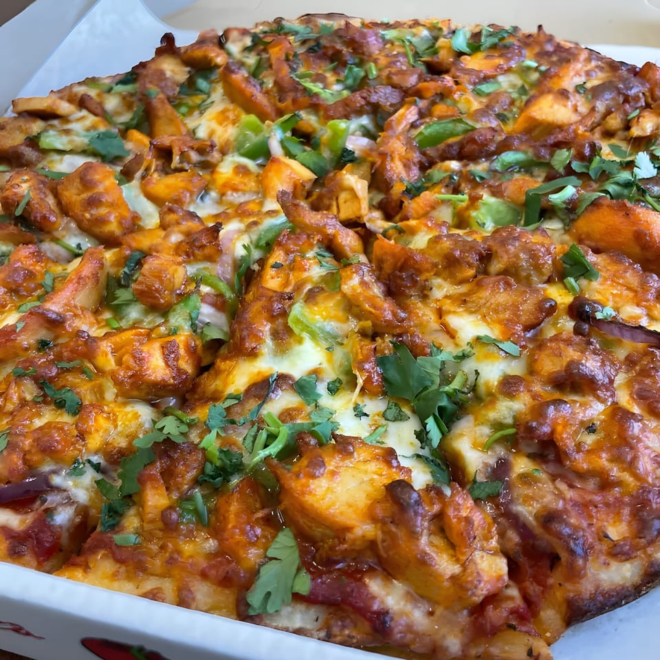 Close-up of a Pizza Station pizza with chicken, green peppers, onions, and cilantro.